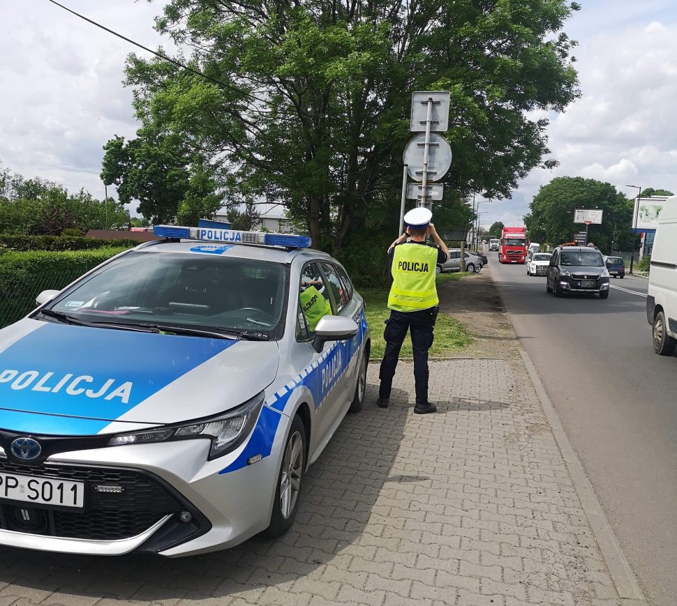 policjant przy radiowozie patrzy przez lornetkę