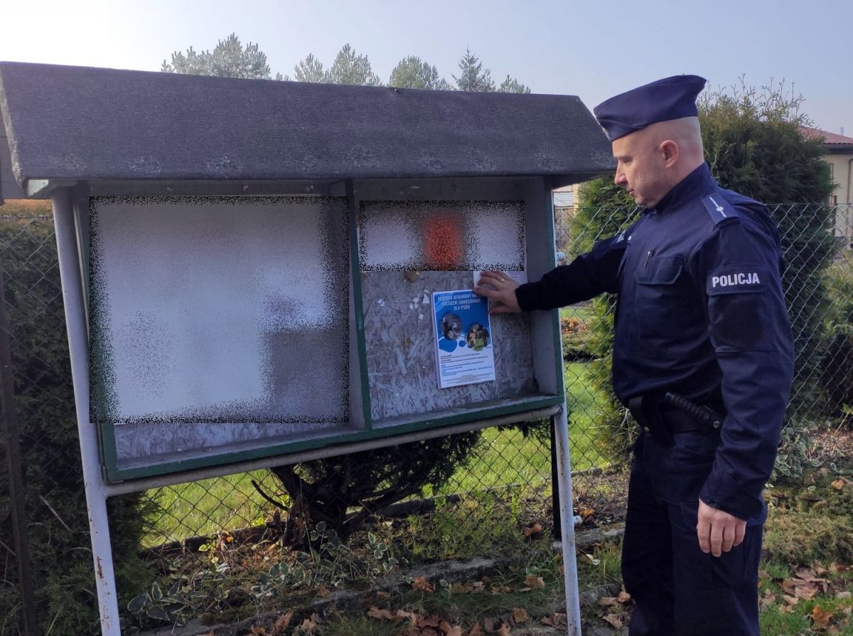 dzielnicowy stoi przy tablicy ogłoszeń i wiesza plakat