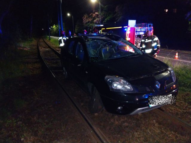 na zdjęciu uszkodzony samochód na torowisku i strażacy, w tle wóz strażacki