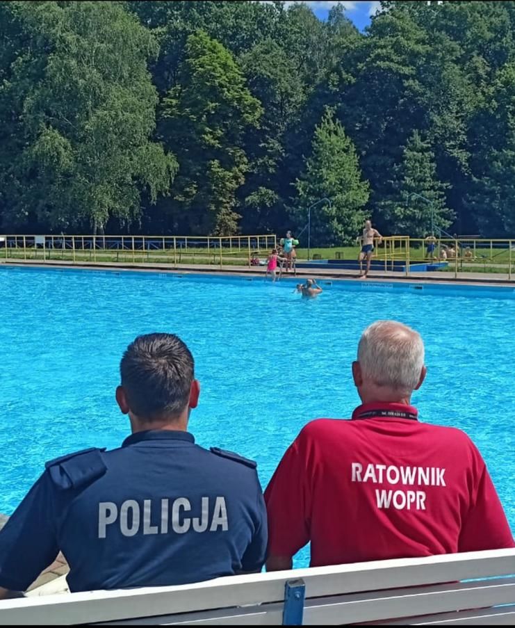 na zdjęciu policjant i ratownik wodny siedzą na ławeczce przy basenie