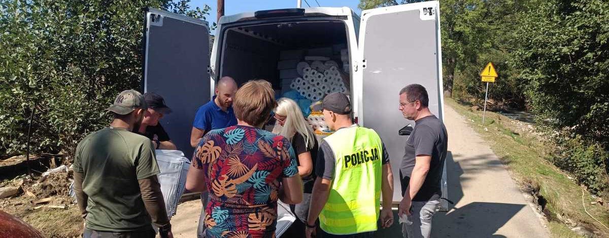 Policjant w kamizelce wśród ludzi przy samochodzie z darami