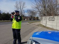 policjant z drogówki stoi na drodze i patrzy przez lornetkę