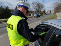 policjant stoi przy samochodzie i wręcza odblaskowe opaski