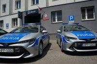 dwa radiowozy stoją przed budynkiem komendy
