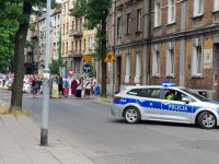 radiowóz blokujący ulicę a za nim przemarsz procesji