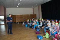 policjant stoi i opowiada dzieciom siedzącym na krzesełkach