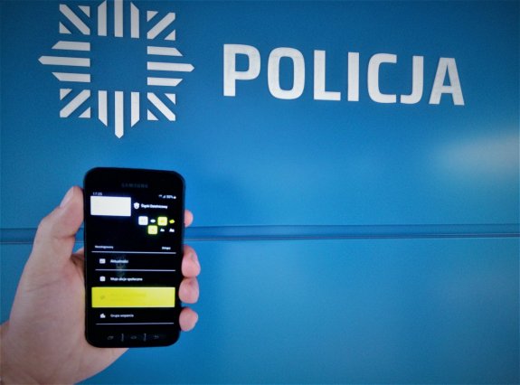 telefon trzymany w ręce na tle napisu Policja