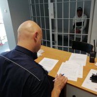 policjant przy biurku i zatrzymany za kratkami
