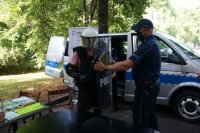policjant i mężczyzna ubrany w kask, kamizelkę, ochraniacze, który trzyma tarczę ochronną