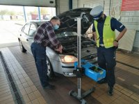 policjant z diagnostą stoją przy aucie z urządzeniem do kontroli oświetlenia