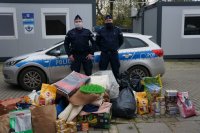 policjanci stoją przy radiowozie i zebranych darach