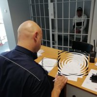 policjant wypełnia dokumentację przy osadzonym zamkniętym za okratowanymi drzwiami