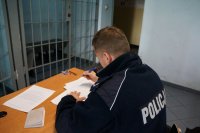 policjant wypisuje dokumentację w pomieszczeniu z kratami