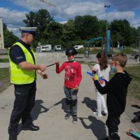 policjant rozdaje dzieciom na hulajnogach odblaski