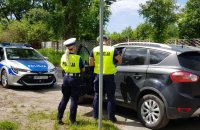 policjant i policjantka wykonują kontrolę przy zatrzymanym pojeździe