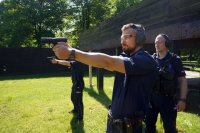 policjant strzela z broni, obok stoi instruktor