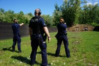 policjanci stoją na strzelnicy z bronią wycelowaną w trenażery, obok stoi instruktor