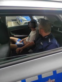policjant w radiowozie siedzi obok podejrzanego