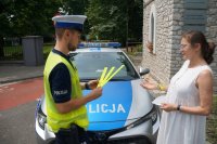 policjant stoi przy radiowozie i wręcza odblaski