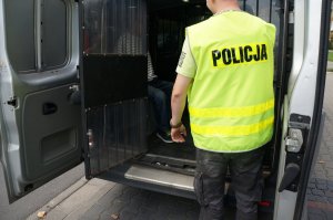policjant stoi przy tylnych drzwiach radiowozu