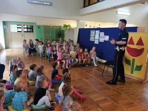 policjant stoi przed dziećmi, które siedzą