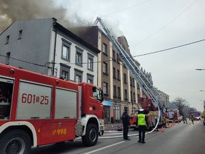 pojazdy straży pożarnej, policjanci przy budynku, na którym pali się dach