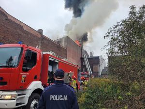 pożar dachu budynku, policjant stoi przed pojazdem straży pożarnej