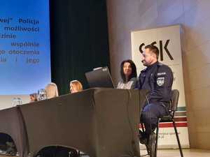 na zdjęciu policjant i kobieta siedzą na scenie przy stole