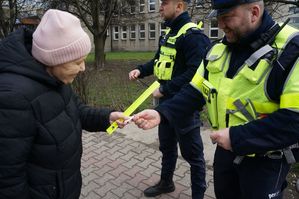 na zdjęciu policjanci wręczają kobiecie opaskę odblaskową