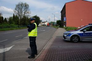 na zdjęciu policjant z drogówki stoi z radarem na drodze, obok radiowóz