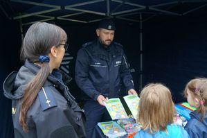 na zdjęciu policjant daje dzieciom książeczki edukacyjne