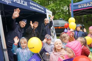 na zdjęciu policjant, strażniczki miejskie i dzieci machają