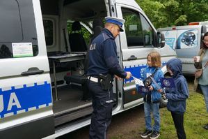 na zdjęciu policjant z drogówki rozdaje dzieciom gadżety profilaktyczne