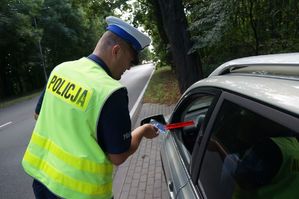 na zdjeciu policjant wręcza opaski odblaskowe i zawieszkę keirującemu