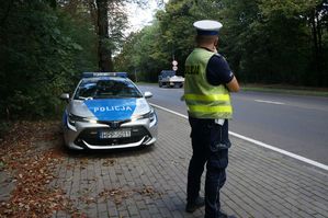 na zdjeciu policjant stoi przy radiowozie