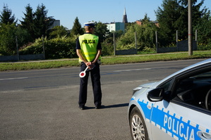 na zdjęciu policjant z drogówki na drodze, obok radiowóz