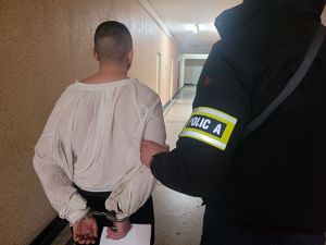 na zdjęciu policjant prowadzi zakutego w kajdanki zatrzymanego