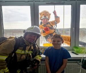 na zdjęciu strażak na oddziale z dzieckiem a za oknem alpinista w przebraniu