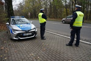 na zdjęciu policjanci z drogówki stoją przy radiowozie