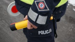 na zdjęciu policjant trzyma urządzenie do sprawdzania stanu trzeźwości oraz tarcze do zatrzymywania pojazdów