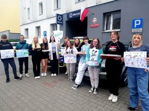 na zdjęciu grupa uczniów z plakatami i ciastami przed budynkiem komendy