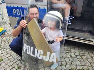 na zdjęciu policjant z przedszkolakiem ubranym w kask, który trzyma tarczę ochronną