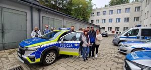 na zdjęciu zdjęcie policjanta i uczestników obok radiowozu