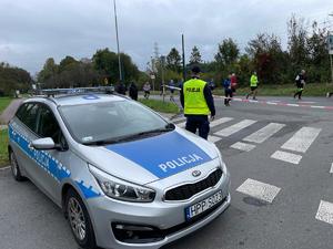 na zdjęciu biegacze, radiowóz oraz policjant