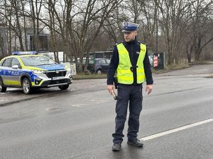 na zdjęciu policjant stoi na drodze, za nim radiowóz