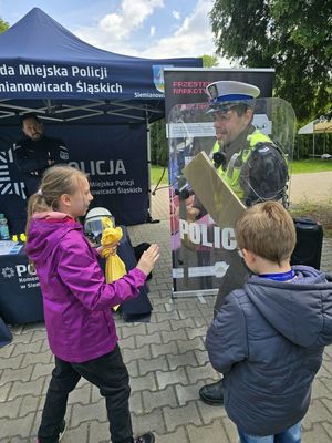 na zdjęciu policjant trzyma tarczę a dzieci ją popychają