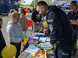 na zdjęciu policjant wręcza dzieciom książeczki