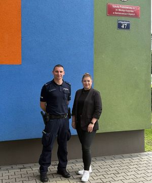 na zdjęciu policjant i pracownica MOPS przed szkołą