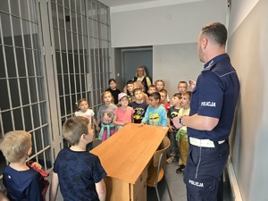 na zdjęciu dzieci z policjantem przy okratowanych drzwiach