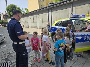 na zdjęciu policjant z dziećmi rozmawia przy radiowozie